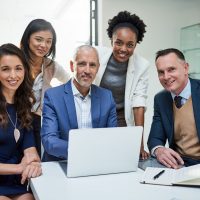 Porträt einer Gruppe von Geschäftsleuten, die zusammen an einem Laptop in einem modernen Büro arbeiten.